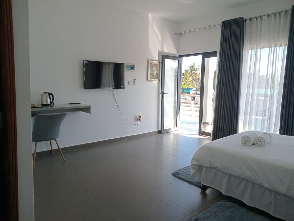Quarto com secretária, televisão e acesso à varanda